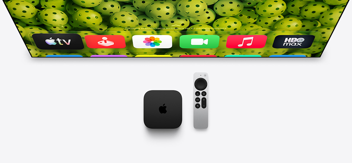 Un Apple TV 4K y un control Siri Remote debajo de un televisor, la pantalla muestralos íconos de las apps de la pantalla de inicio en la fila superior sobre un fondo verde con pelotas de pickleball