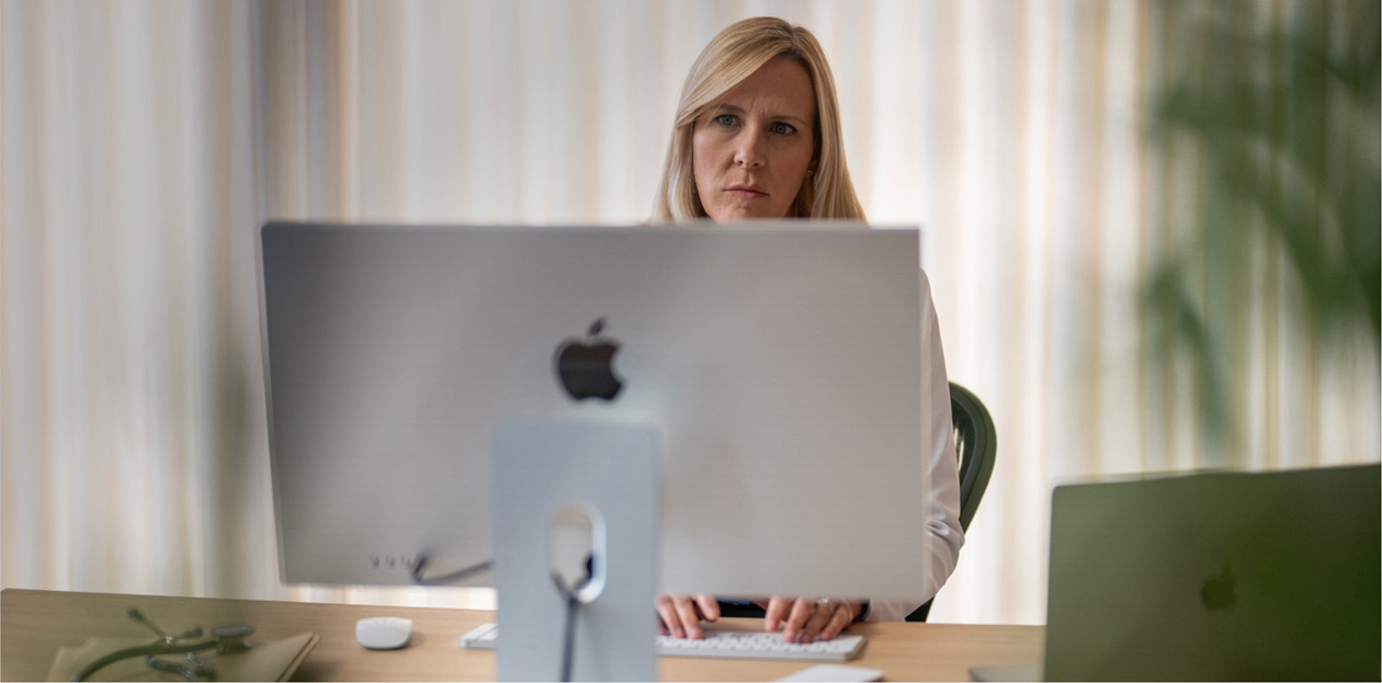 En sundhedsmedarbejder sidder ved sit skrivebord og kigger på en iMac-skærm.