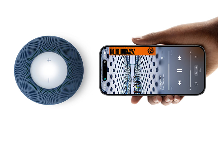 HomePod mini 2 et iPhone : une main tient un iPhone à côté d’un HomePod mini 2 bleu pour la fonctionnalité Handoff