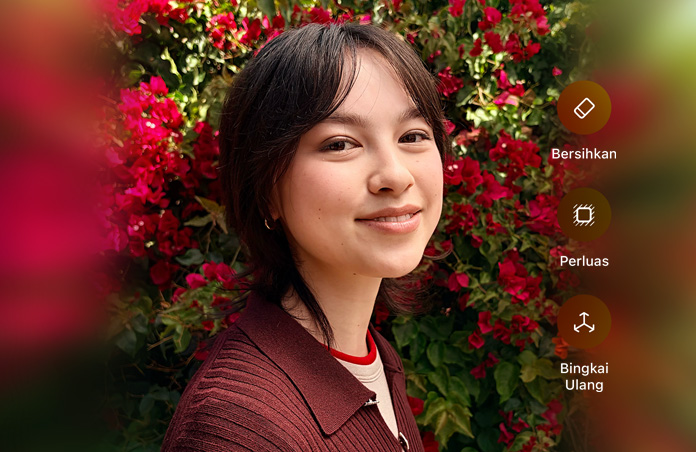Foto seseorang berambut cokelat yang sedang tersenyum, mengenakan sweater cokelat, dikelilingi bunga merah, demo pengeditan foto AI dengan opsi Bersihkan, Perluas, Bingkai Ulang yang ditampilkan di atas foto