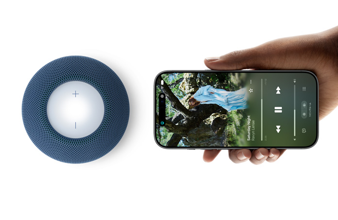 HomePod mini 2とiPhone：片手で持ったiPhoneがブルーのHomePod mini 2の横にあり、Handoff機能を使っている