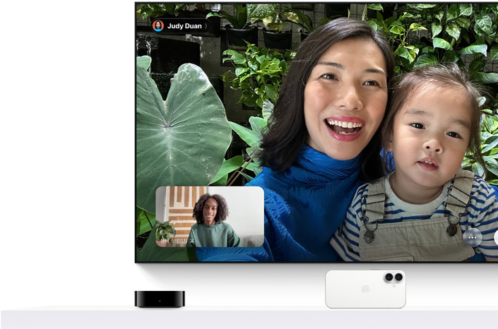 Apple TV 4K와 iPhone: TV 화면에 FaceTime 통화가 떠 있고, 한 사람이 어린 아이를 안고 있고, 두 번째 발신자가 별도 창에 보입니다