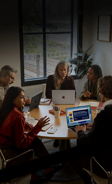 Cinq personnes assises autour d’une table de conférence, travaillant ensemble sur des MacBook, avec des iPhone face vers le bas sur la table