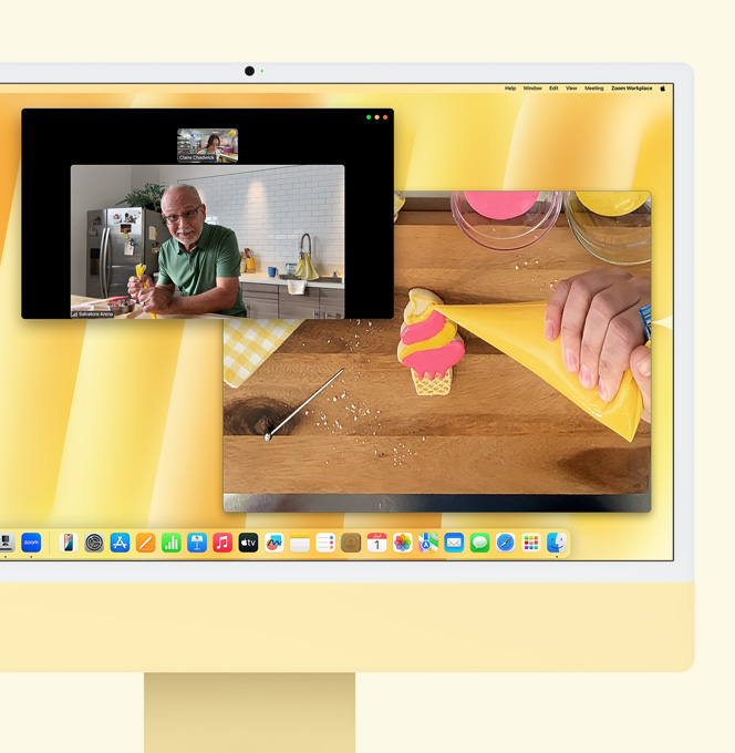 iMac باللون الأصفر. عرض توضيحي لميزة العرض الرأسي. شاشة تعرض صانعة حلويات تشارك في مكالمة فيديو مع شخص آخر. وتعرض إحدى الشاشتين صانعة الحلويات ووجه الرجل، بينما تعرض الشاشة الأخرى يدي صانعة الحلويات وهي تزيّن قطعة بسكويت