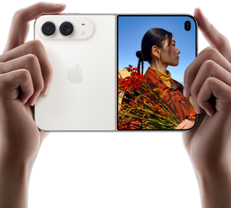 جهاز iPhone Duo، لون أبيض النجوم، يدان تحملان الجهاز في الوضع الأفقي، مفتوح، اللوحة اليسرى تعرض نظام كاميرا مزدوجة 48MP Fusion، اللوحة اليمنى تعرض شخصاً تُلتقط صورته على الشاشة الخارجية، يمكن لهذا الشخص رؤية وجهه لأن الصورة تُلتقط باستخدام ميزة Duo Preview