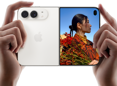iPhone Duo v nebeskej bielej farbe, držia ho dve ruky v orientácii na šírku, je rozložený, na ľavom paneli vidno 48 Mpx zadné kamery Dual Fusion, na pravom paneli vidno na vonkajšom displeji fotografovanú osobu, ktorá vďaka funkcii Duo Preview vidí pri fotení svoju tvár