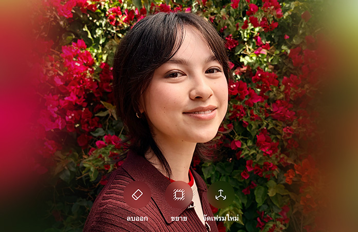 รูปภาพบุคคลที่มีผมสีน้ำตาลกำลังยิ้มแย้ม, สวมเสื้อสเวตเตอร์สีน้ำตาล, ล้อมรอบด้วยดอกไม้สีแดง, การสาธิตการปรับแต่งภาพถ่ายด้วย AI พร้อมตัวเลือกในการลบออก ขยาย และจัดเฟรมใหม่ที่แสดงอยู่เหนือภาพ