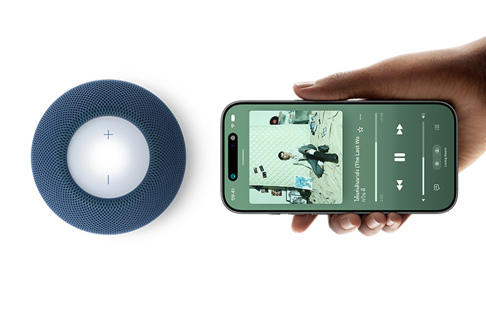 HomePod mini 2 และ iPhone: มือข้างหนึ่งถือ iPhone ในแนวนอนอยู่ข้างๆ HomePod mini 2 สีน้ำเงินเพื่อใช้คุณสมบัติ Handoff