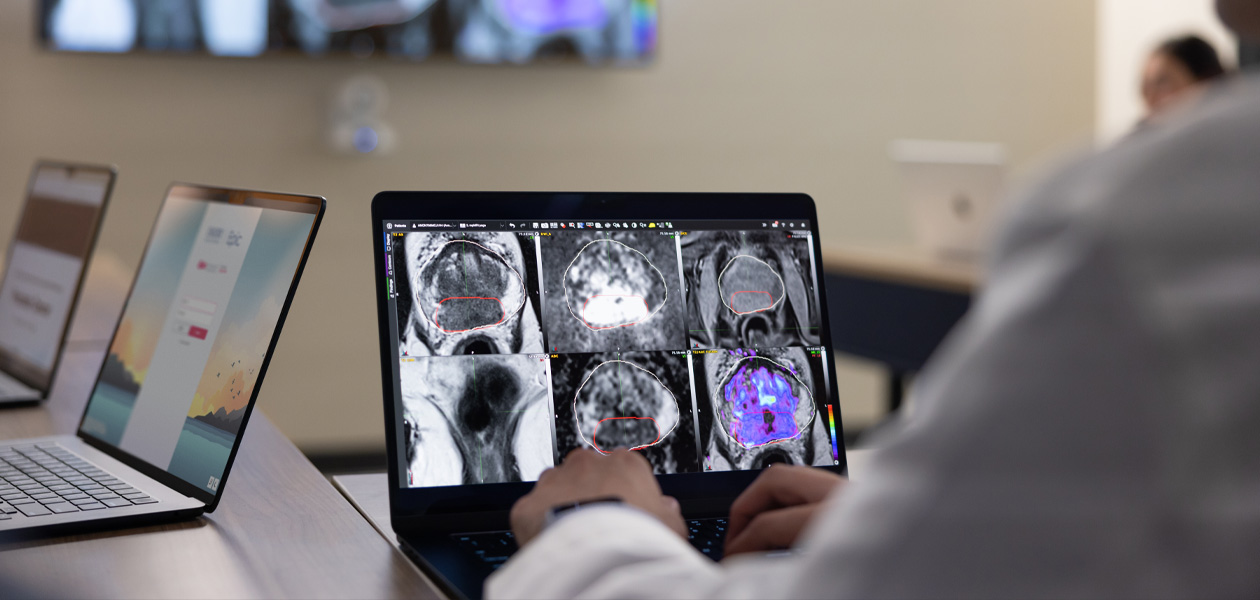Eine Person prüft medizinische Scans auf einem MacBook. Zwei weitere MacBook Geräte stehen geöffnet im Hintergrund.