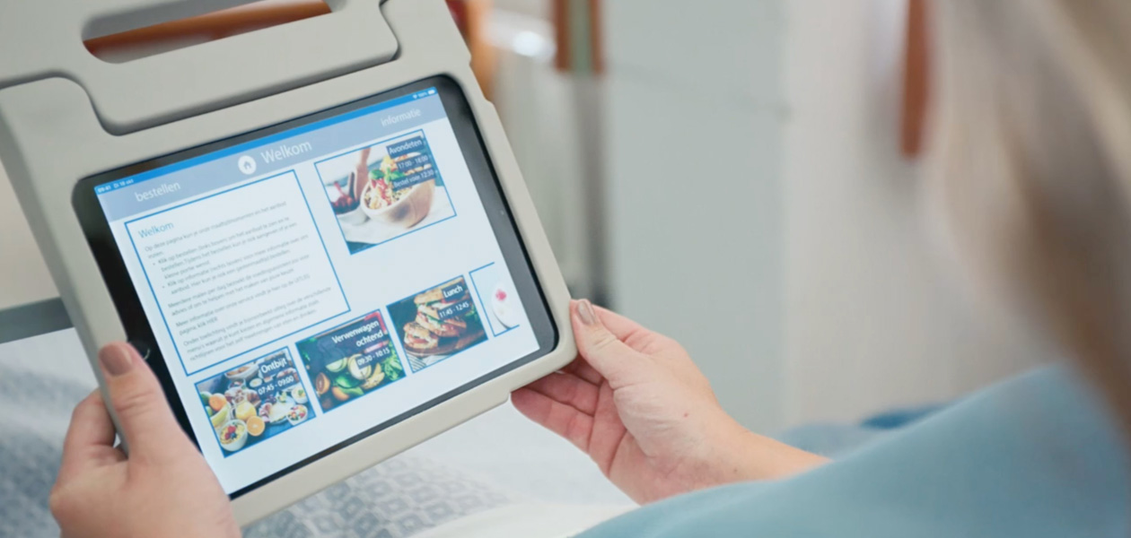 Eine Patientin sitzt in ihrem Krankenbett und schaut auf ein iPad Display.