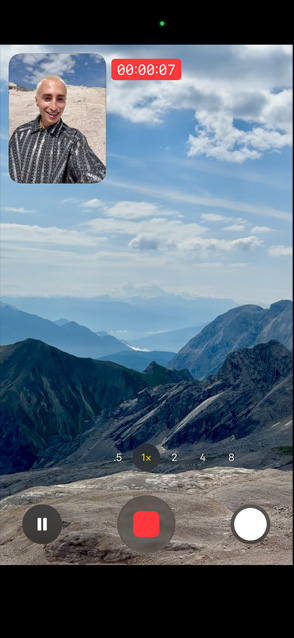 一個人在示範雙向同拍錄影，他用前置相機拍攝自己，同時用後置相機拍攝風景秀麗的山脈