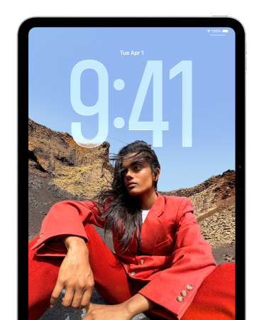 iPad menampilkan Layar Terkunci di mana angka berukuran besar yang menunjukkan waktu terlihat di belakang gambar seseorang yang sedang duduk