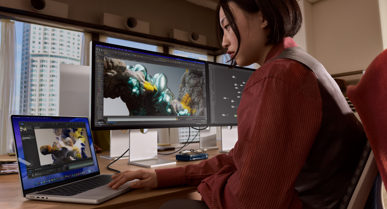 Una persona en una oficina trabaja en un notebook MacBook conectado a un monitor Studio Display XDR mediante un puerto Thunderbolt 5